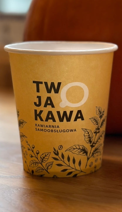 Kubek papierowy z żółtym nadrukiem „TW JA O KAWA” i motywem roślinnym