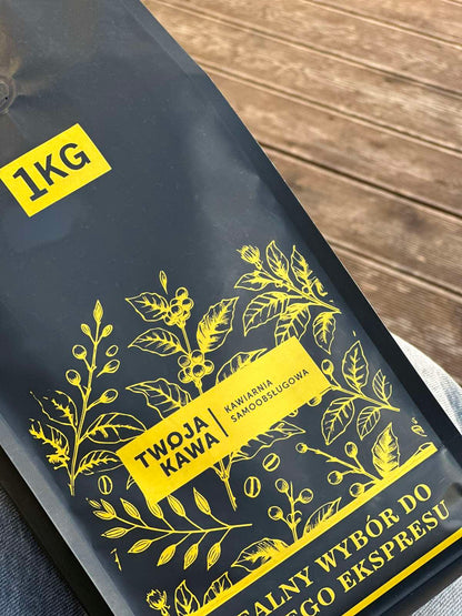 Worek z ziarnistą kawą specialty 1 kg, ciemny z żółtym motywem roślinnym.